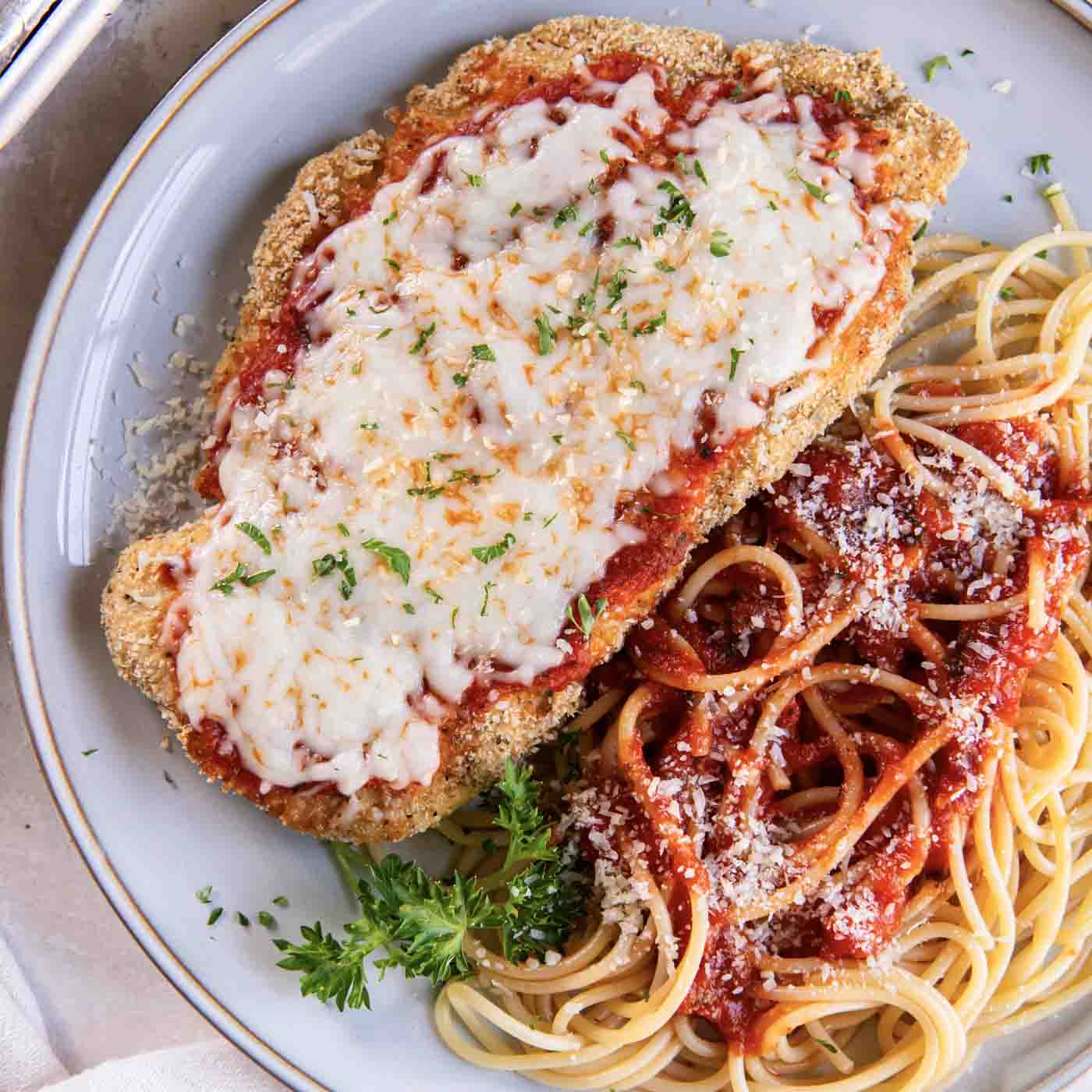 Breaded chicken parmesan topped with tomato sauce and melted mozzarella beside spaghetti
